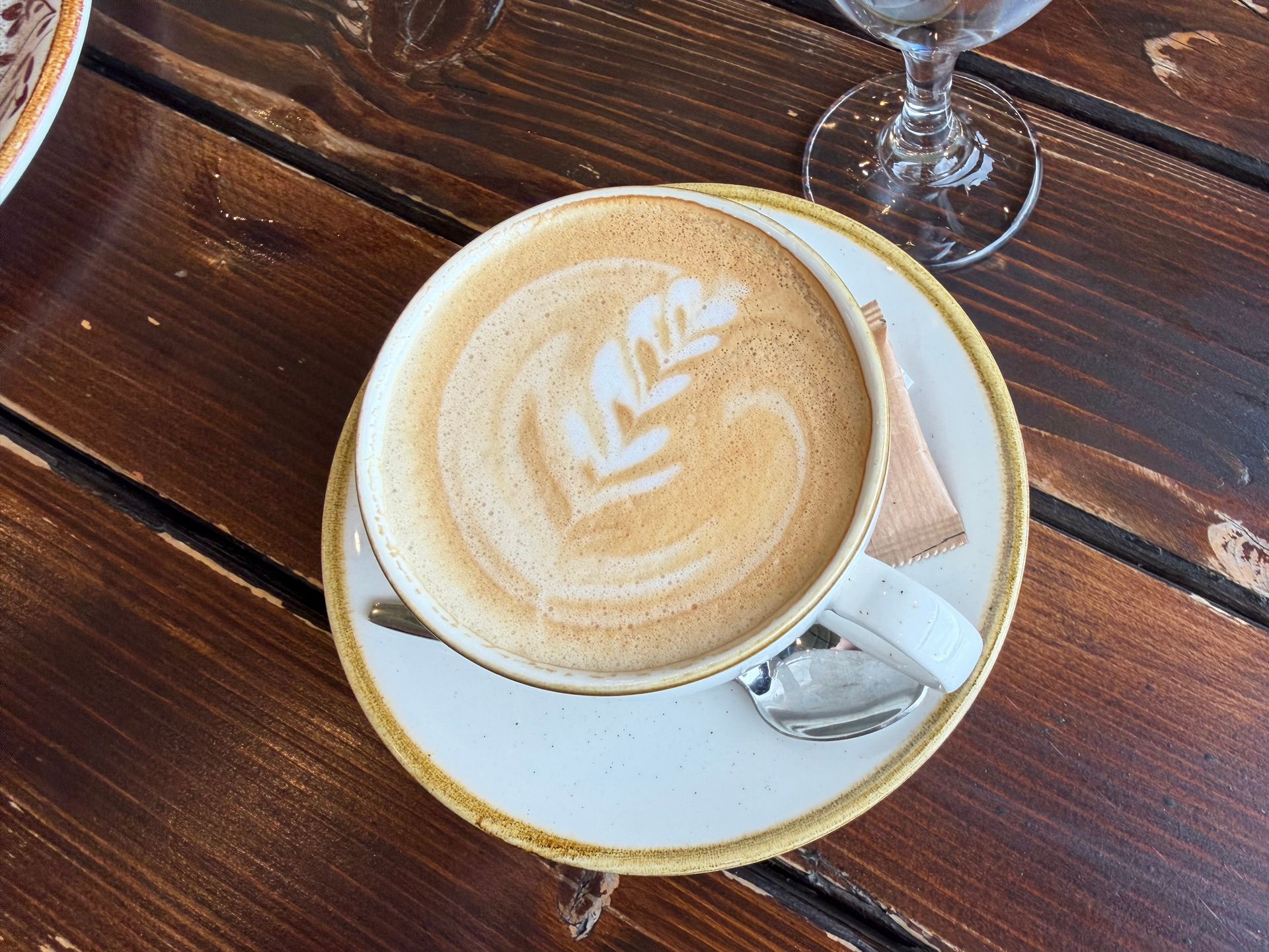 Latte in a white cup on a saucer, with a spoon, on a wooden café table.