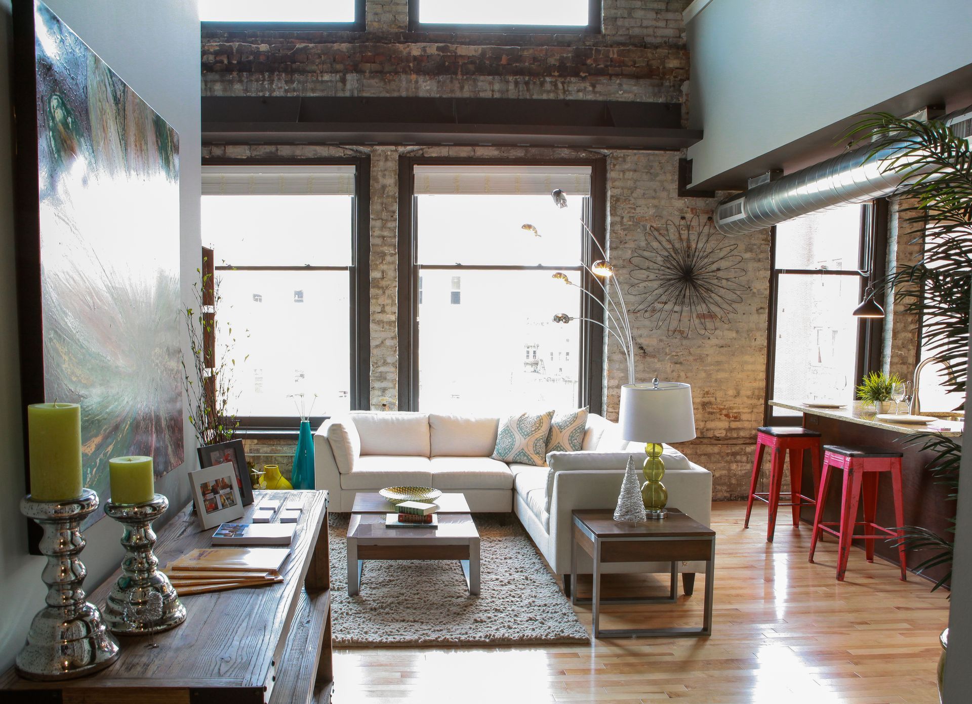 Bright loft living room with white sofa, red barstools, large windows, and wooden floors