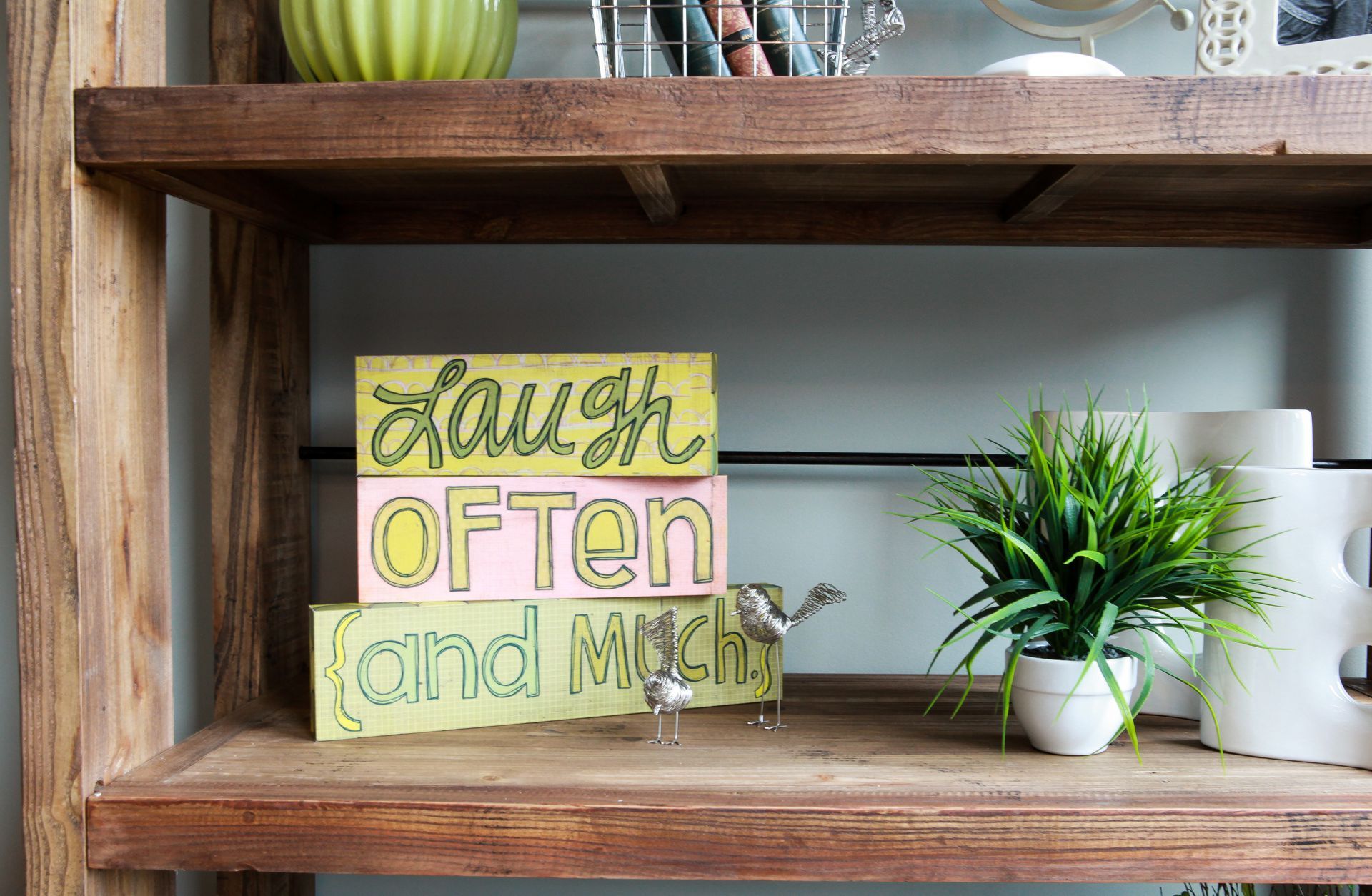 Rustic shelf with “laugh often and much” sign, potted plant, and white canisters