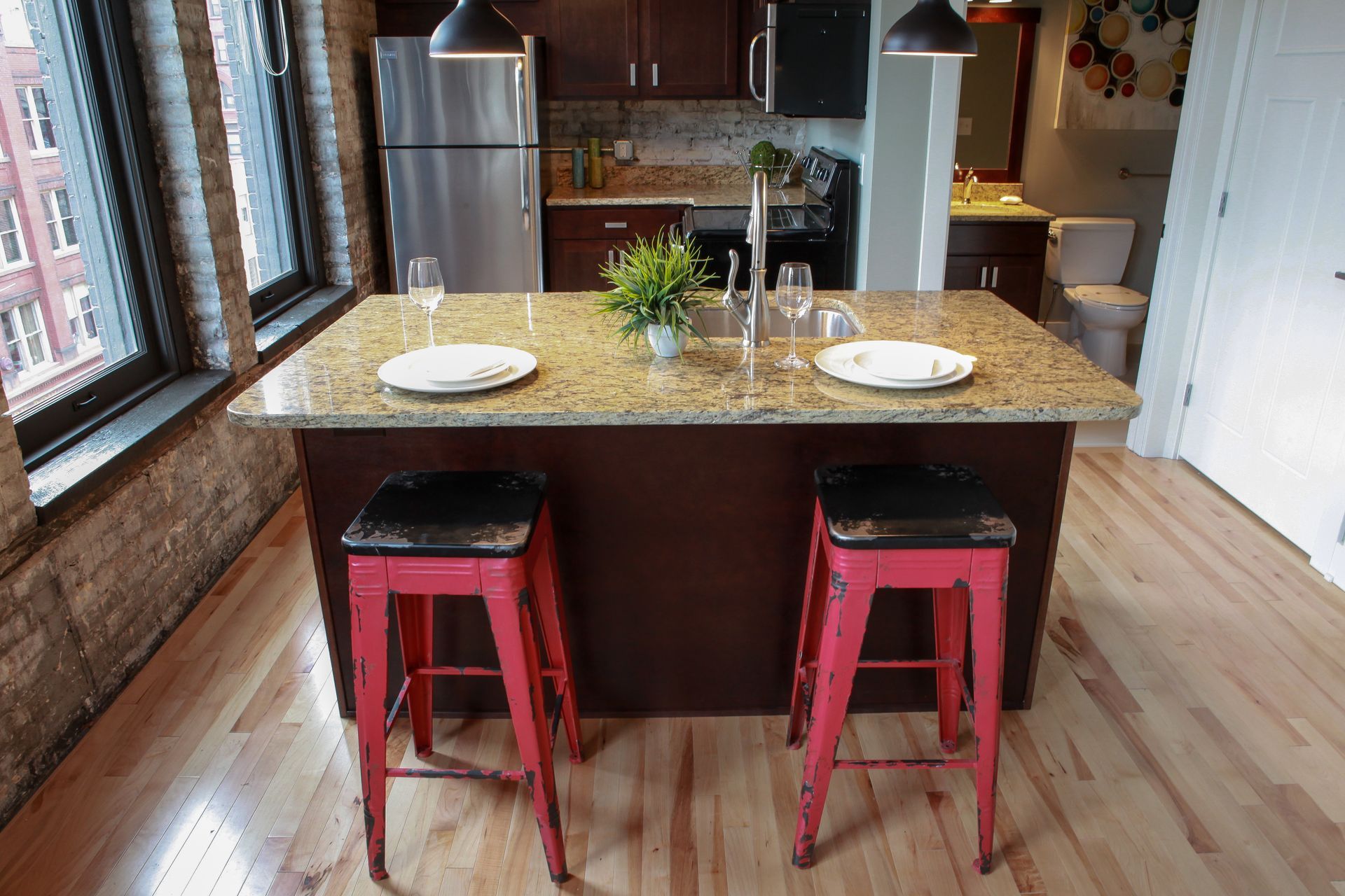 Kitchen island with two red stools, granite countertop, and place settings in a bright modern kitchen