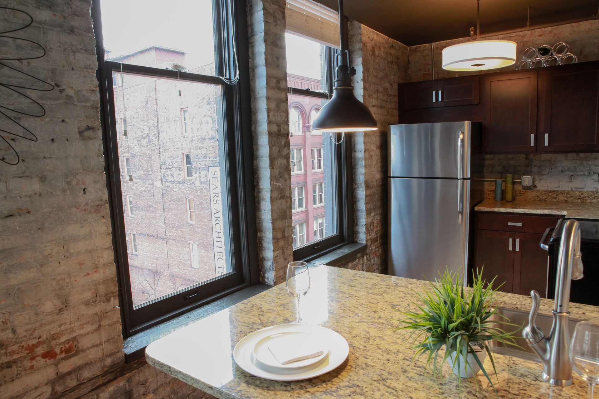 Modern kitchen with large windows, granite island, pendant light, and stainless steel fridge