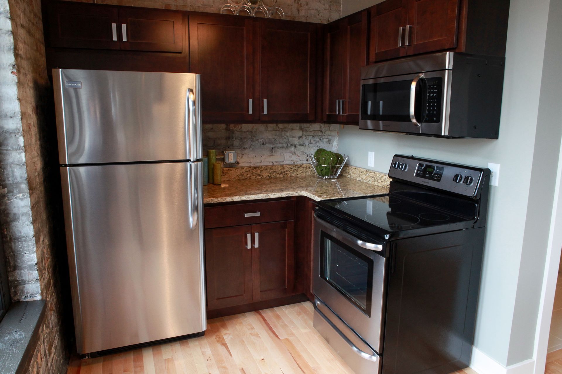 Compact kitchen with stainless steel fridge, black stove, microwave, and dark wood cabinets
