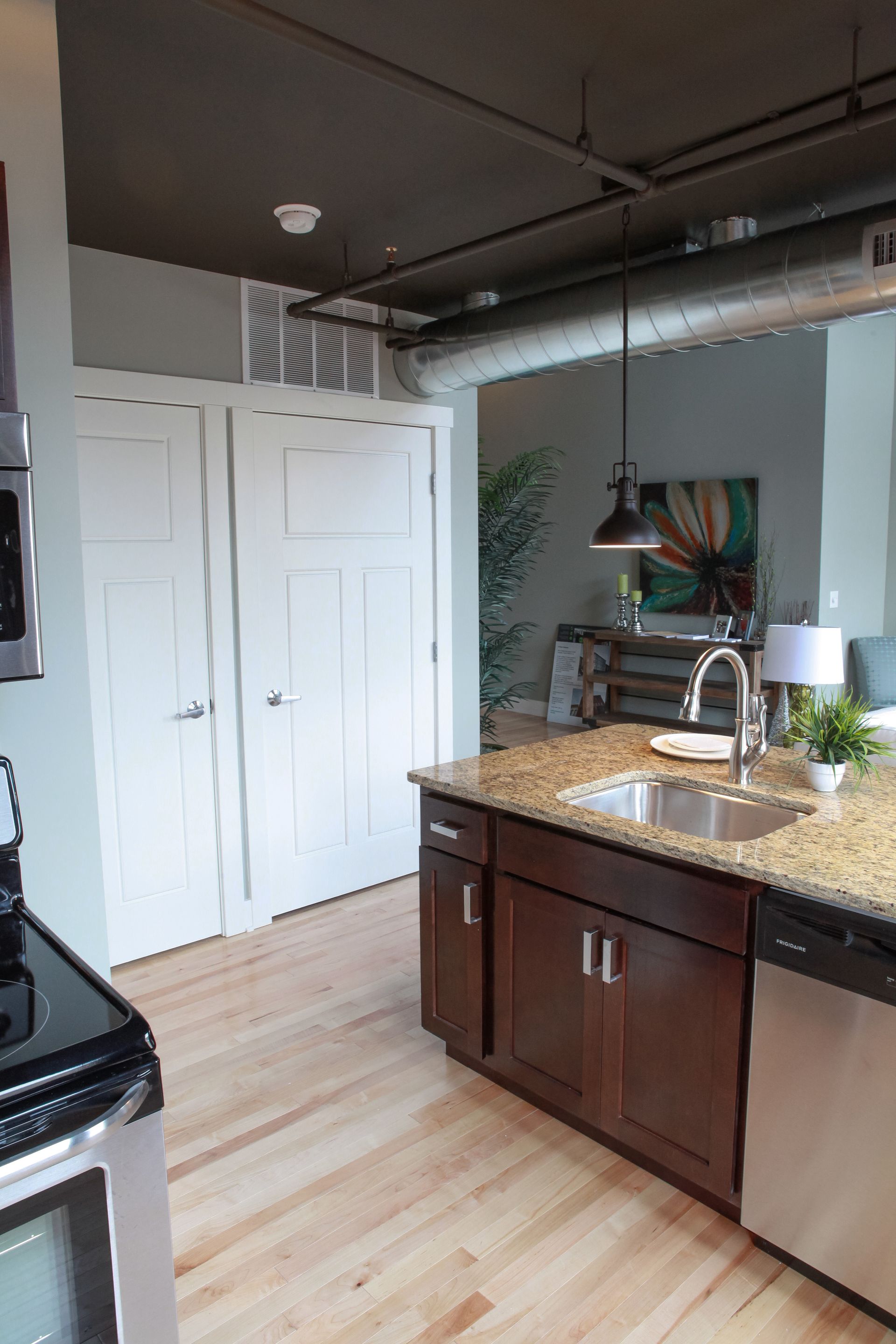 Modern kitchen with dark cabinets, granite counter, stainless sink, white doors, and light wood flooring