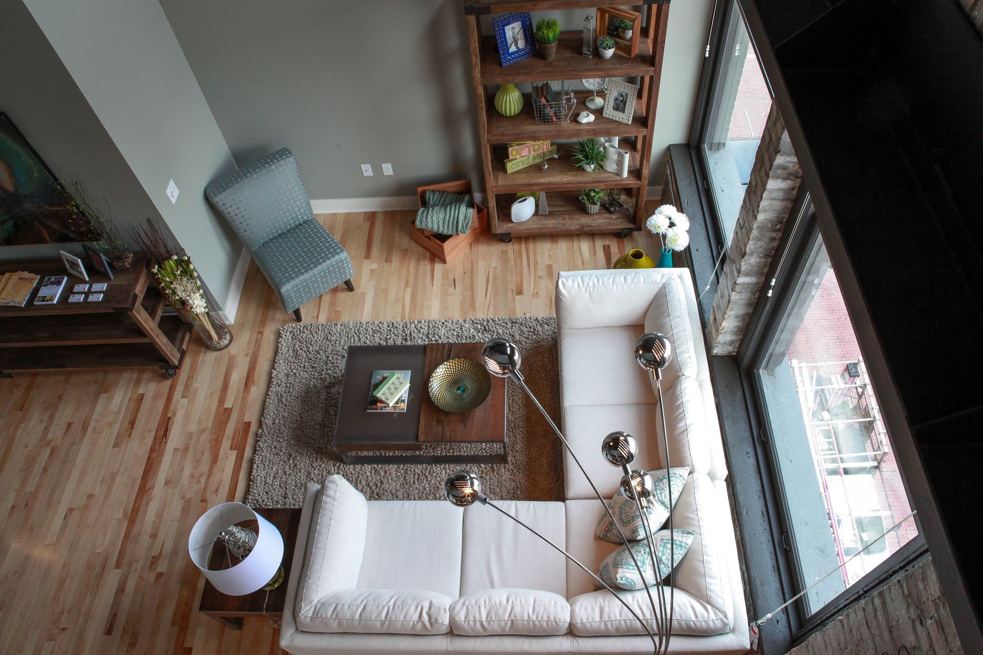 Top-down view of a cozy living room with a white sectional sofa, coffee table, wooden floors, and large windows