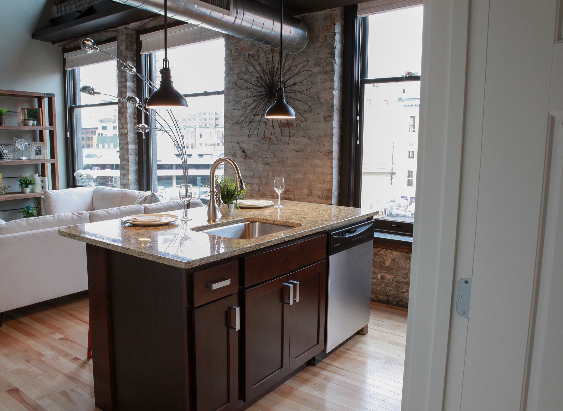 Modern kitchen with a dark island, pendant lights, exposed brick wall, and large windows
