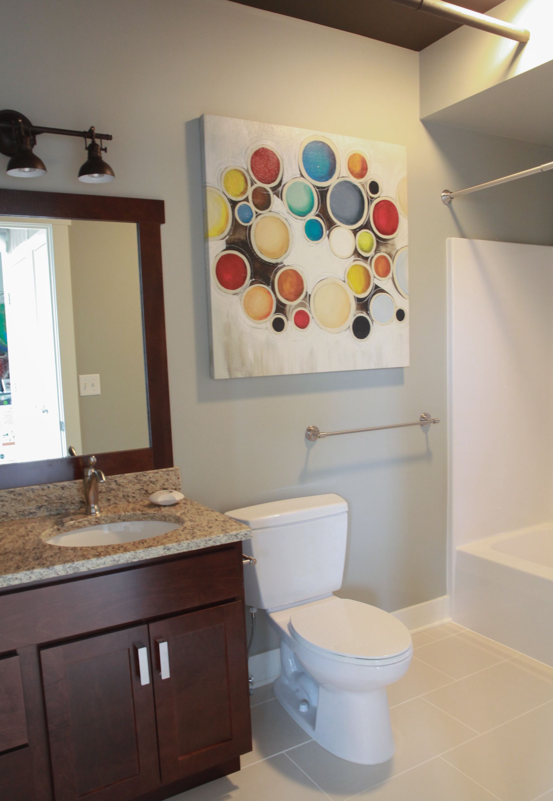 Modern bathroom with toilet, vanity, shower, and colorful wall art