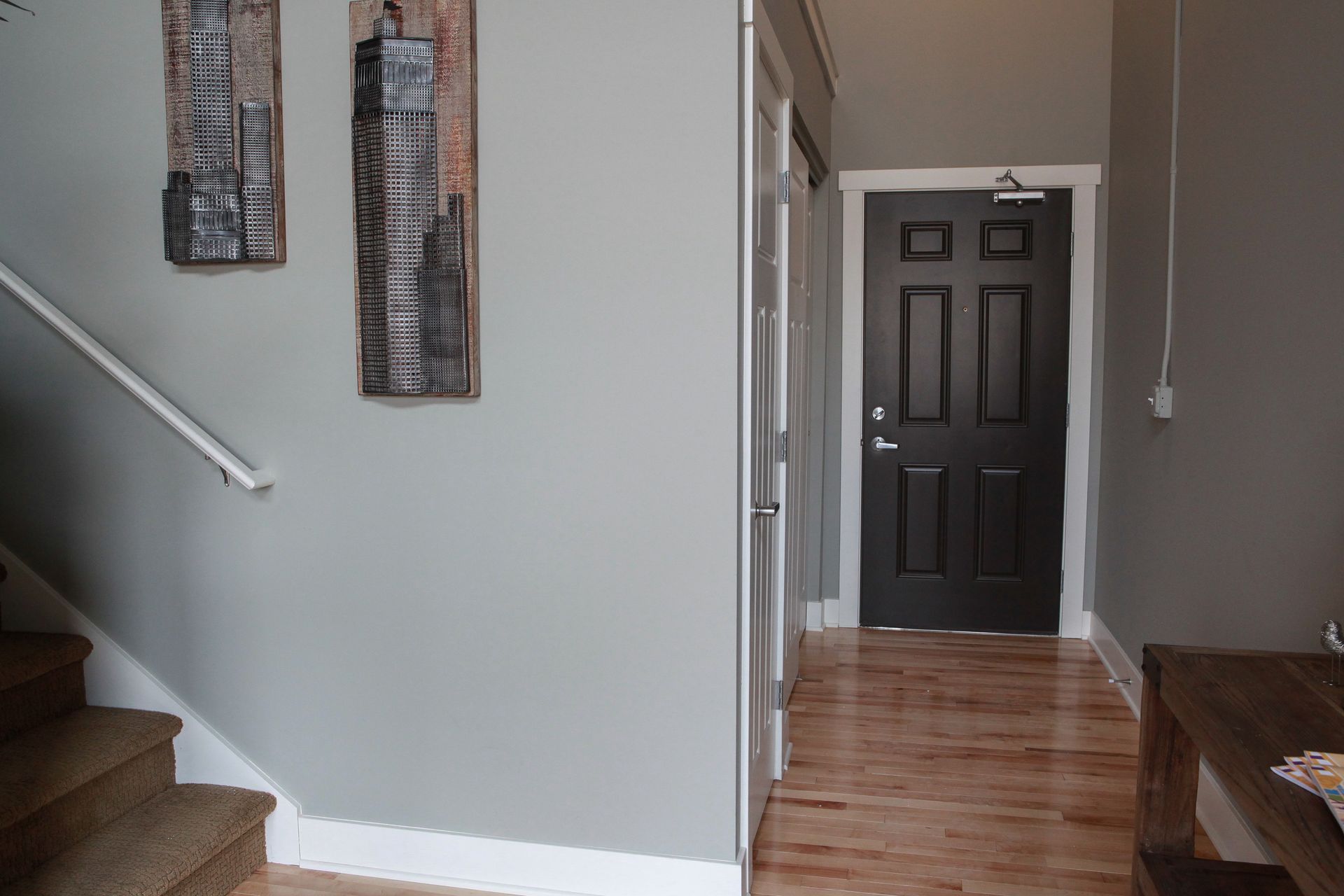 Hallway with staircase, gray walls, wood floor, and dark front door at the end