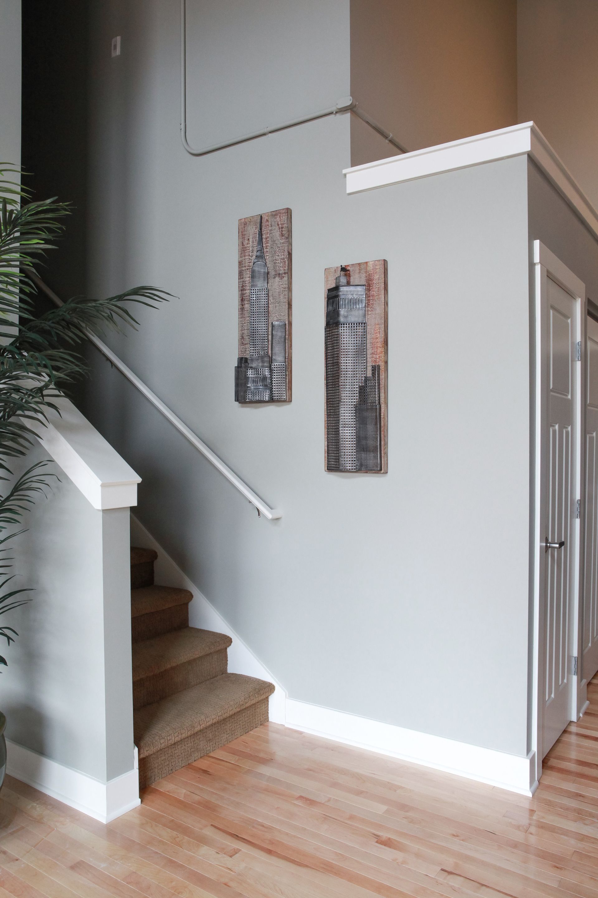 Interior staircase with white walls, wood floor, and two narrow wall art pieces beside a doorway.