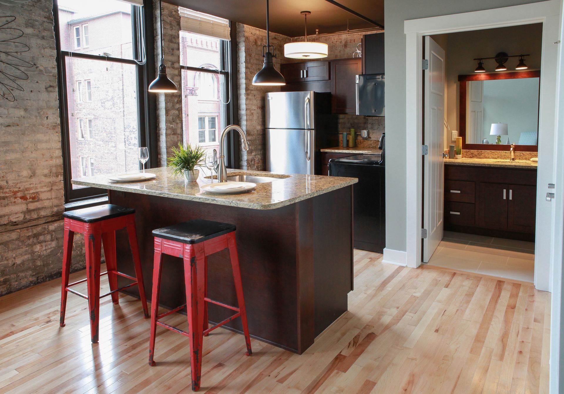 Modern kitchen with dark island, red stools, stainless fridge, and light wood floors.