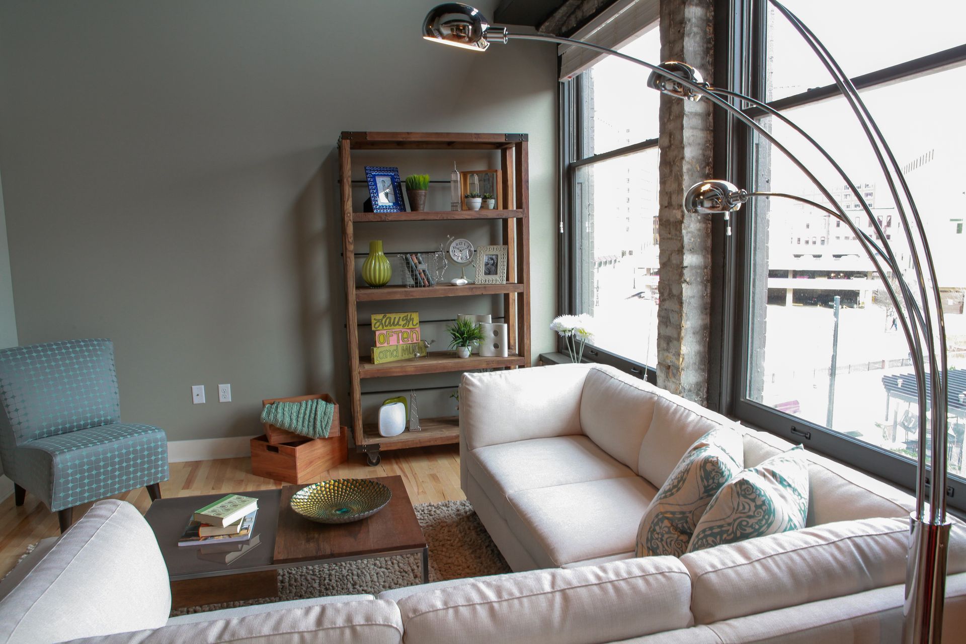 Bright living room with beige sofa, wooden coffee table, bookshelf, and large windows overlooking snow outside