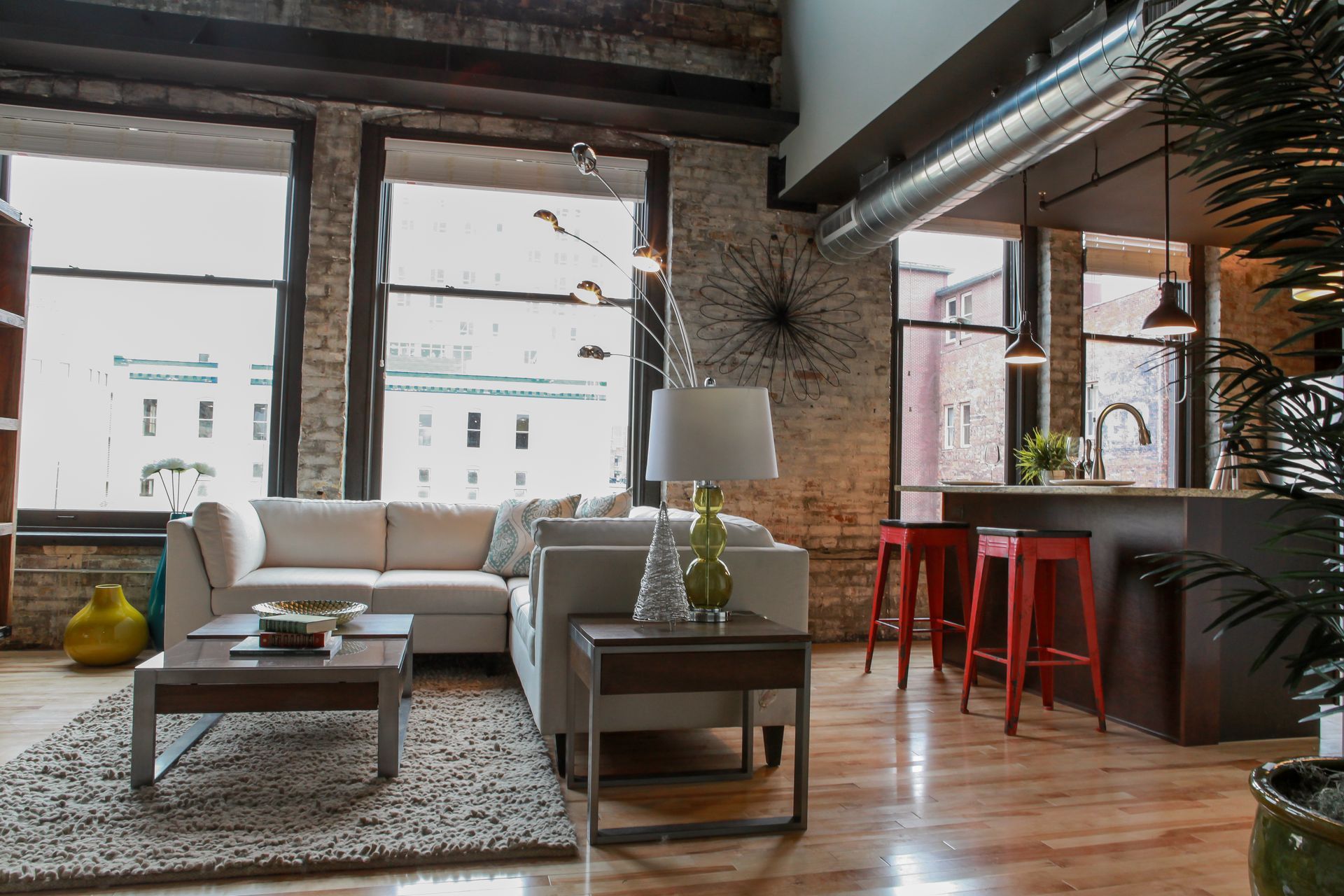 Loft living room with a white sofa, coffee table, red stools, and exposed brick walls
