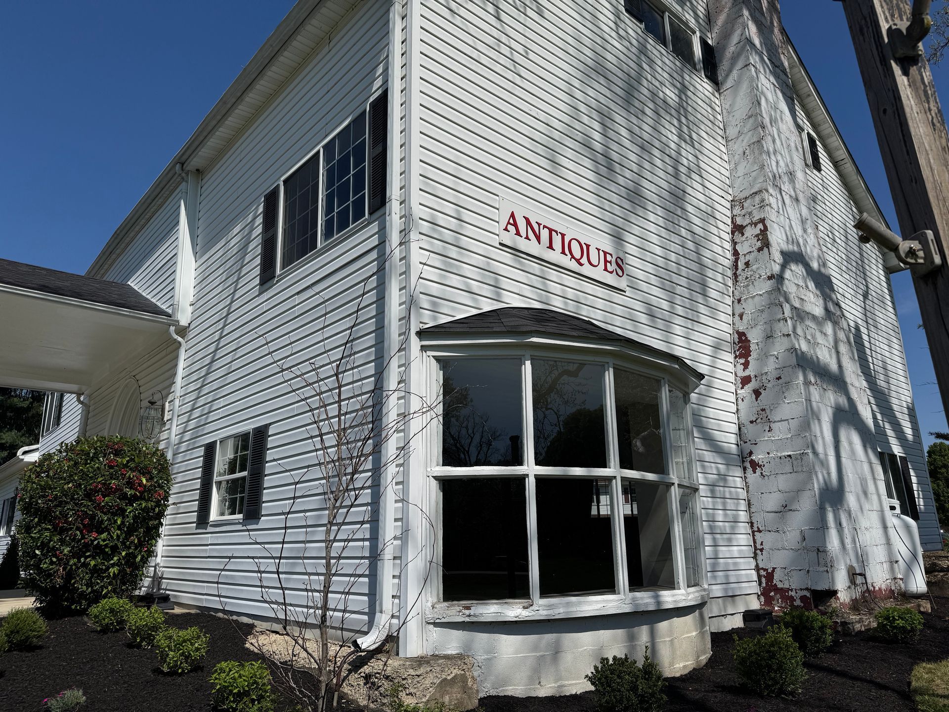 A two-story brick house with a wrap-around porch, gray roof, and attached garage, set in a sunny, tree-lined yard.