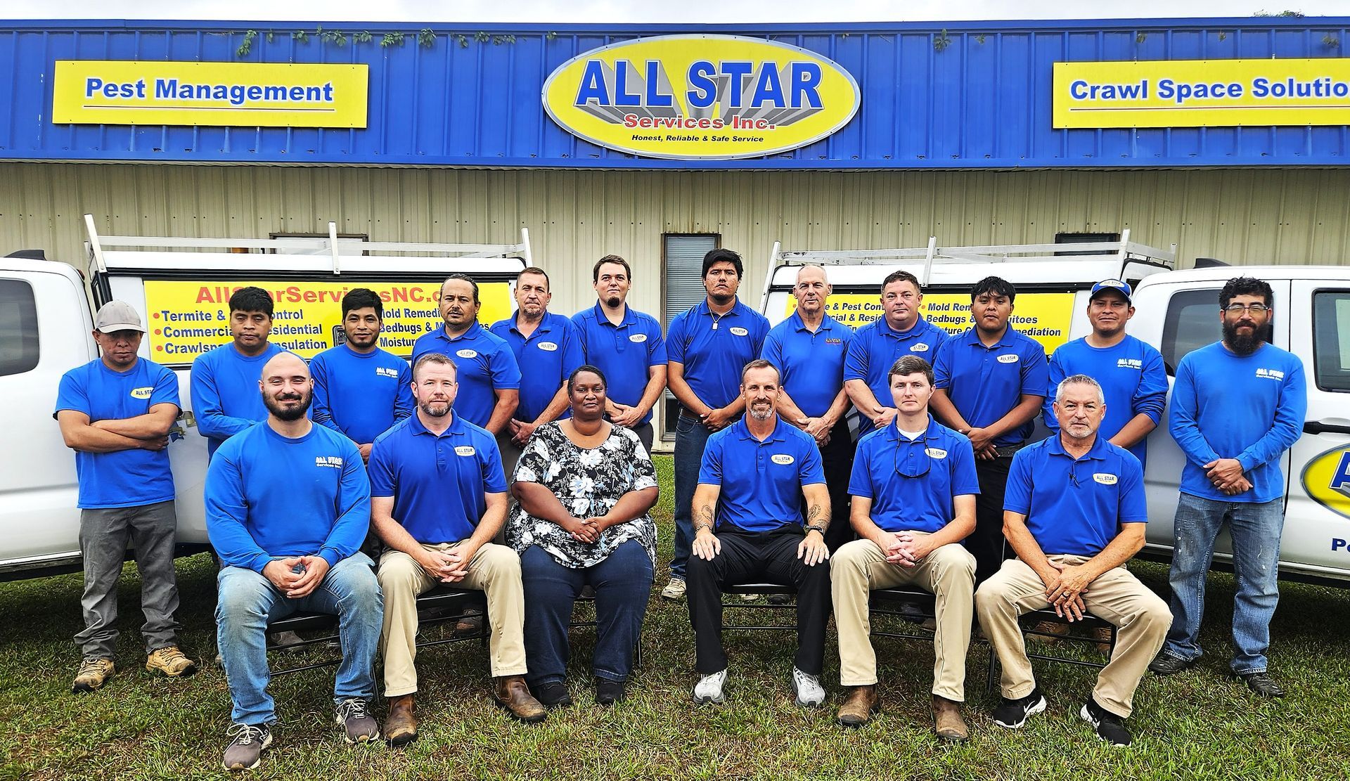 A group of employees in blue company shirts stand together in front of an All Star facility with service vehicles.