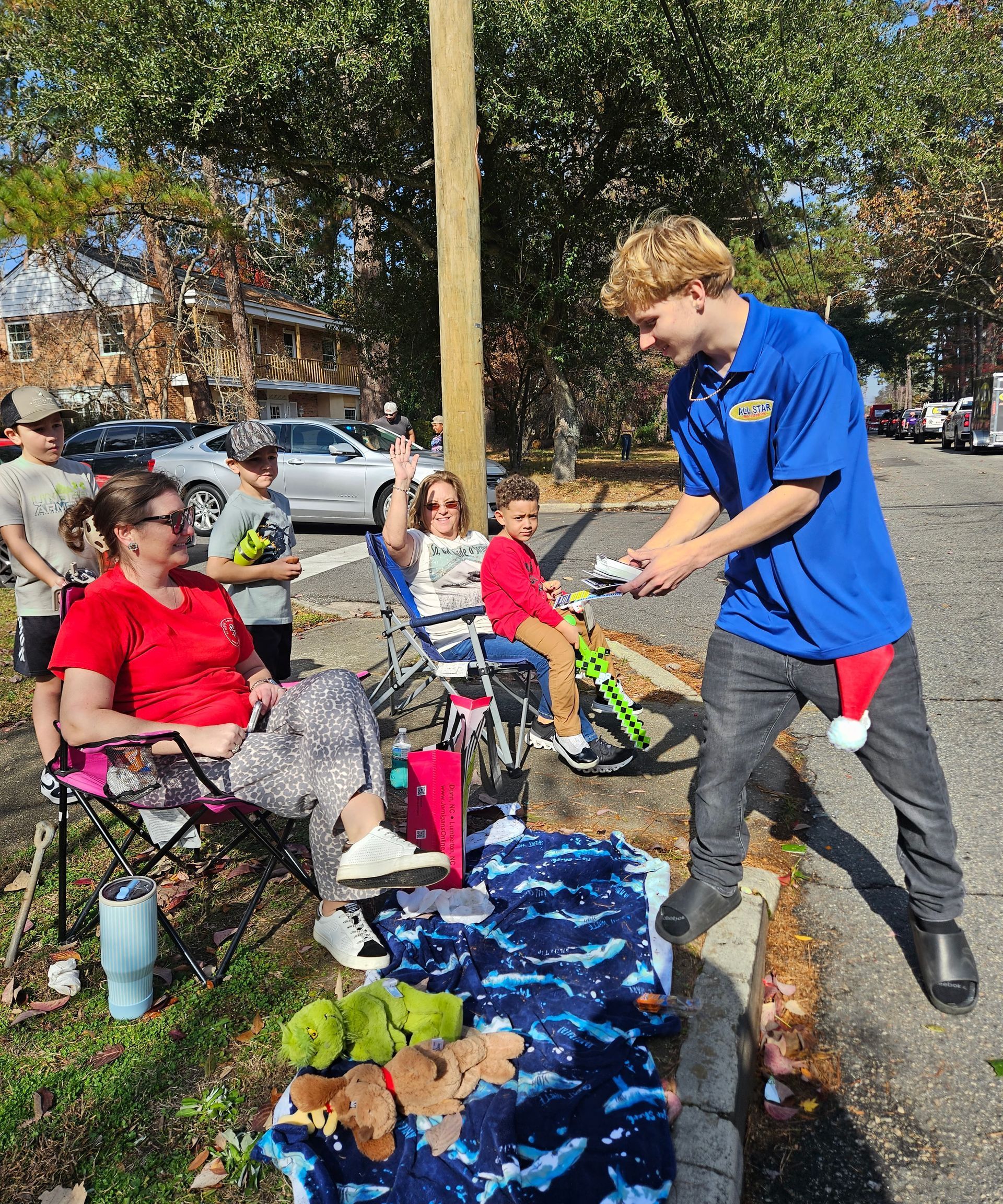 A person in a blue shirt hands a gift to a child in a stroller as others watch during an outdoor parade or event.
