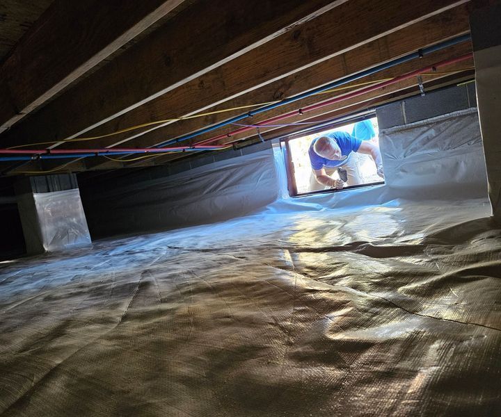 A crawl space encapsulated with white vapor barrier, viewed through an opening where a person is working.