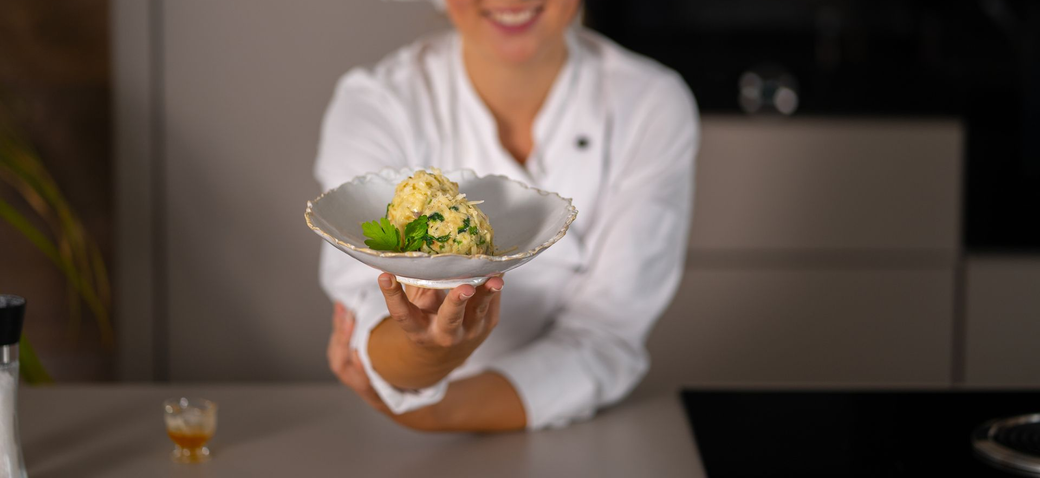 Una persona sorridente con indosso un camice bianco da chef presenta un piatto di cibo.