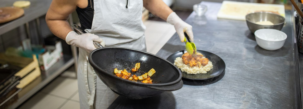 Uno chef impiatta il cibo in una cucina commerciale, utilizzando delle pinze per disporre il pasto su un piatto.