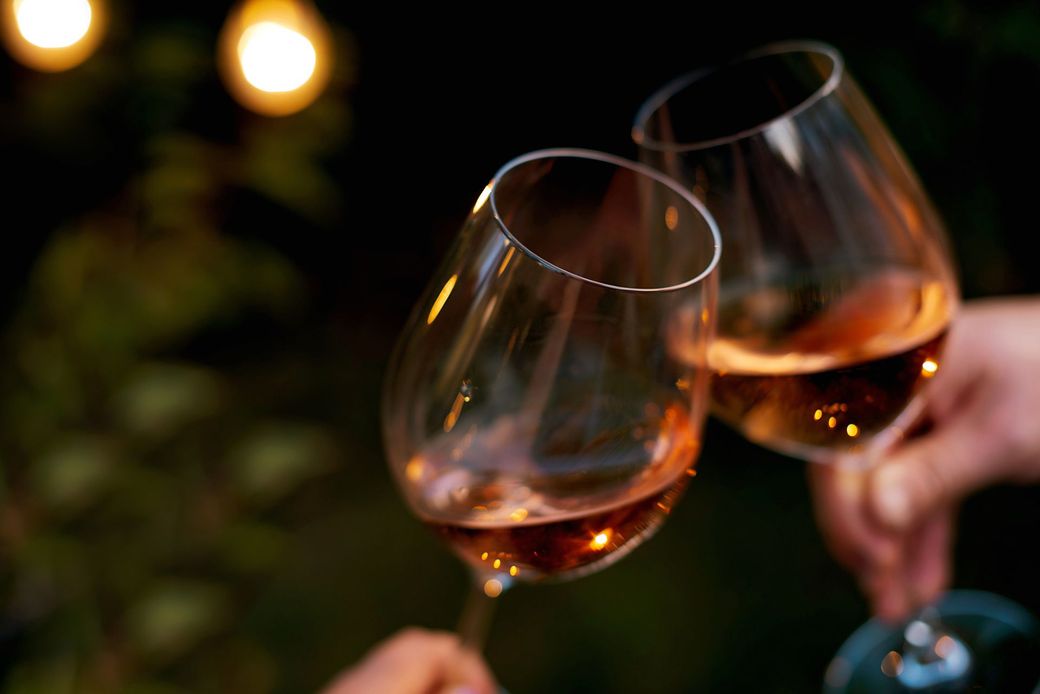 Due bicchieri di vino rosato tintinnano durante un brindisi, sullo sfondo sfocato di un paesaggio esterno.
