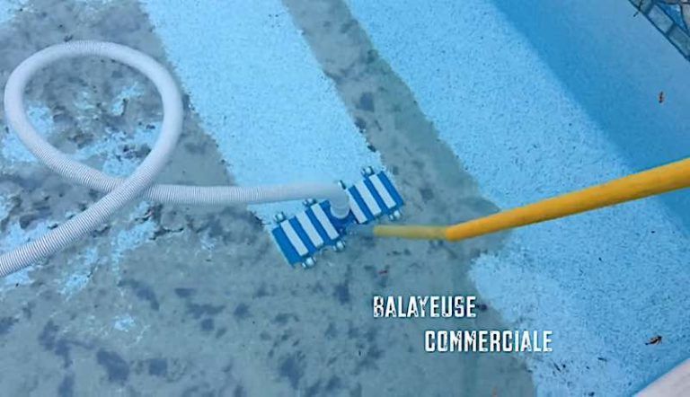 A blue commercial pool vacuum head with a white hose and yellow pole cleaning dirt from the floor of a swimming pool.
