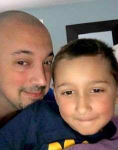 A man and a young boy smiling together for a close-up selfie indoors.