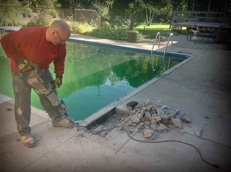 A person using a jackhammer to break up concrete around the edge of a swimming pool.