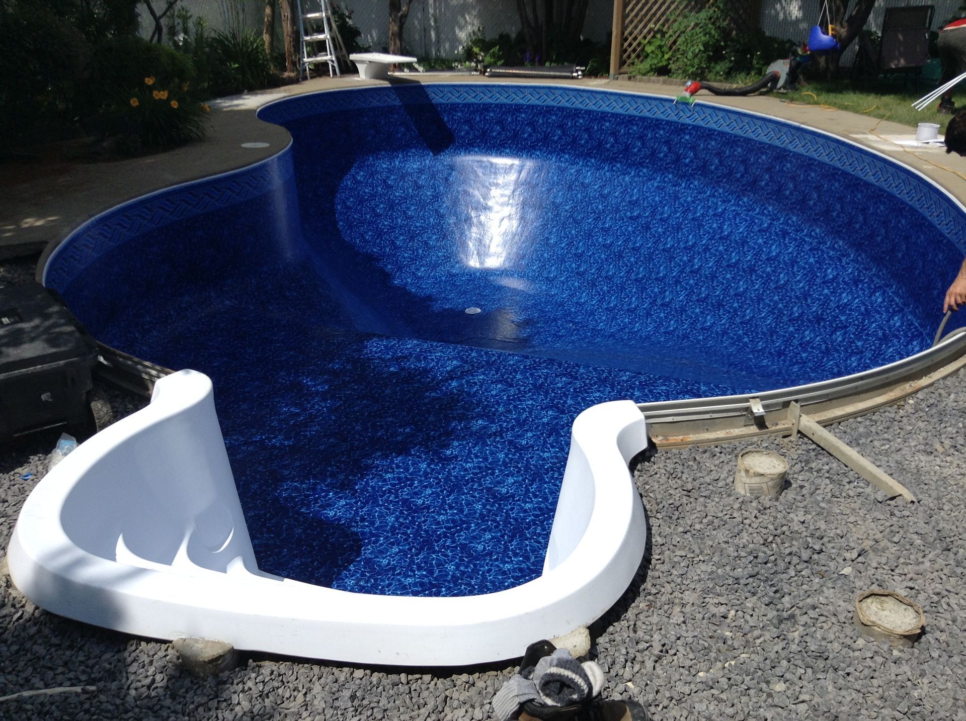 Piscine bleue avec toboggan blanc dans un jardin gravillonné, vue d'en haut