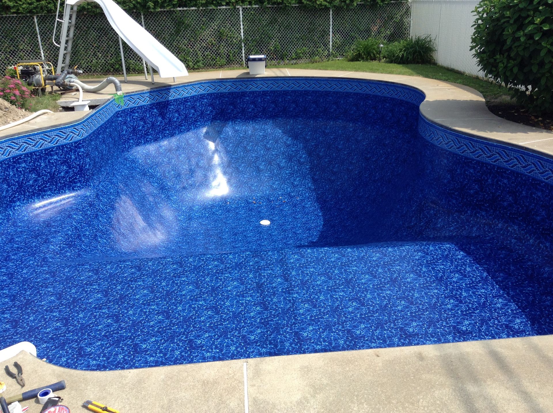 Piscine bleue à l'eau scintillante dans un jardin, bordée de béton et entourée de verdure.