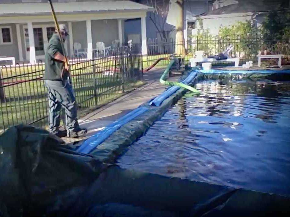 Un ouvrier pose une bâche bleue pour piscine à côté d'une piscine et d'une clôture dans un jardin.