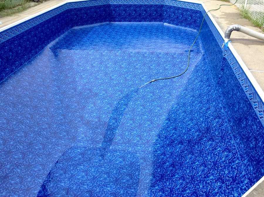 Piscine vide carrelée de bleu, avec un tuyau d'arrosage posé sur le fond asséché.