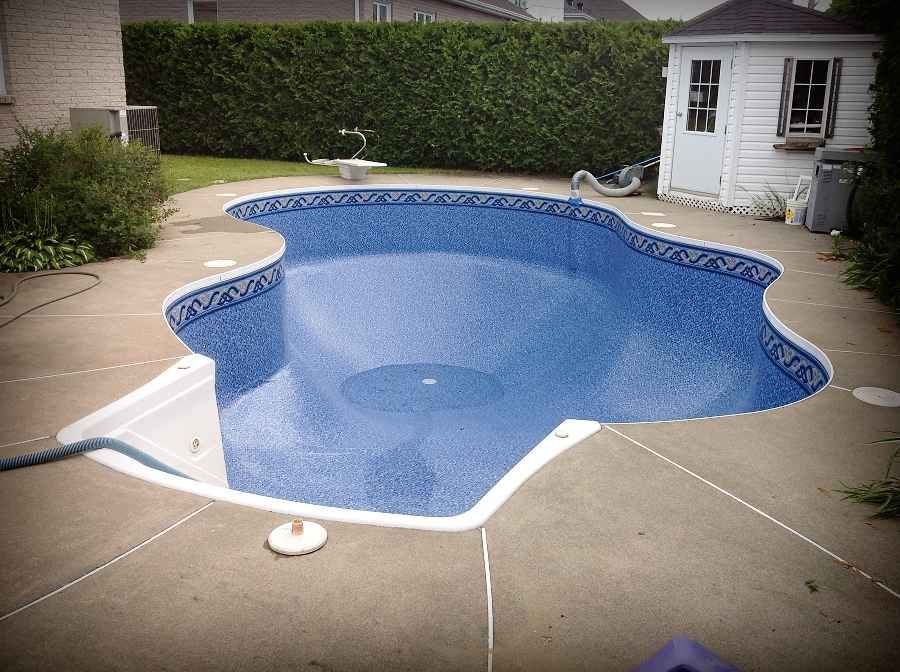 Piscine creusée bleue vide dans une cour arrière avec terrasse en béton beige et abri de jardin blanc