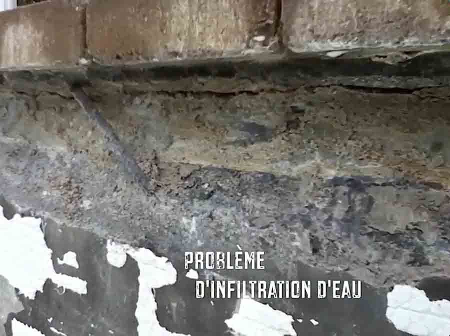 Un mur de maçonnerie endommagé présentant des infiltrations d'eau, avec un plâtre qui s'écaille et un mortier apparent et friable sous la maçonnerie.