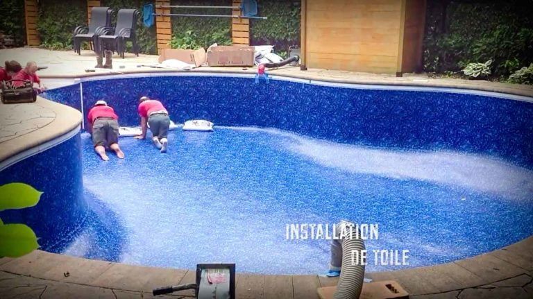 Two people installing a blue patterned liner in an empty backyard swimming pool.