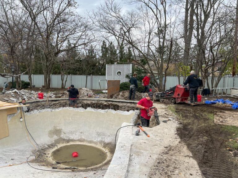 Plusieurs ouvriers sont en train de démolir et de rénover une piscine en béton vide dans la cour arrière d'une maison résidentielle.