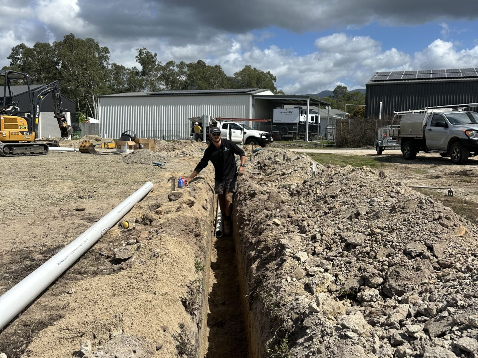 Man in Trench Pointing at Pipes; Construction Site With Dirt, Buildings, and Machinery — HFB Plumbing & Gas in Wrights Creek, QLD