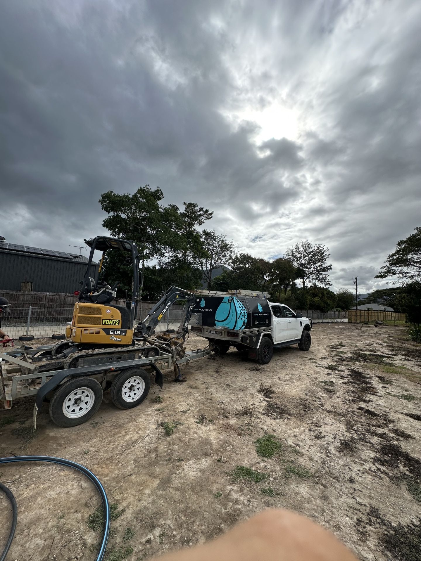 Yellow Excavator on a Trailer Being Towed by a White Truck on a Cloudy Day — HFB Plumbing & Gas in Wrights Creek, QLD