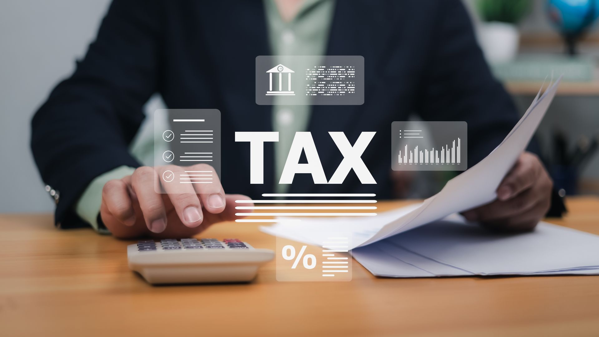 Person calculating taxes with documents, calculator, and overlaid graphics.