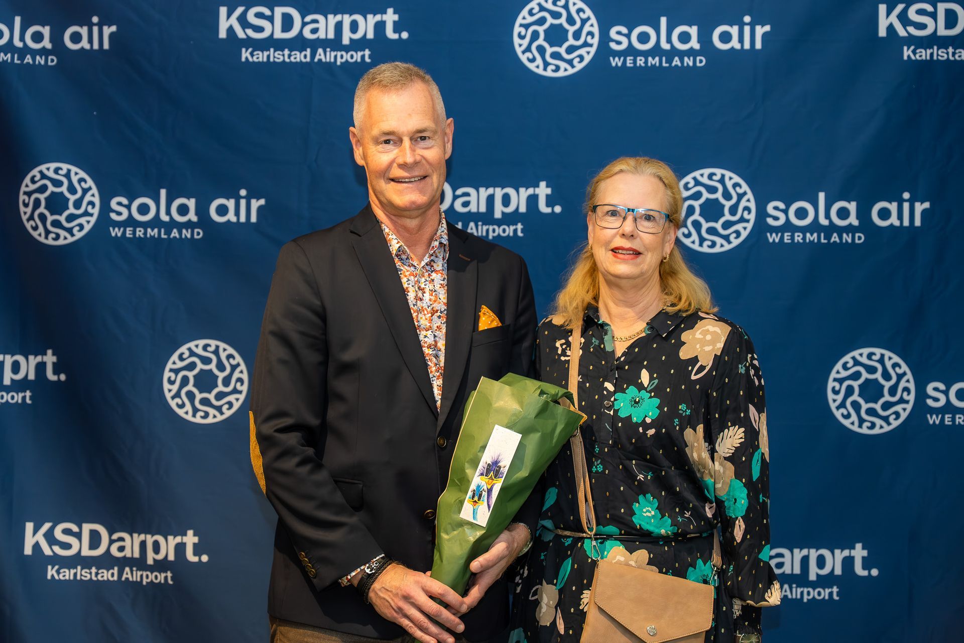 Två personer poserar med en bukett framför en KS Darpt. och Sola Air-bakgrund
