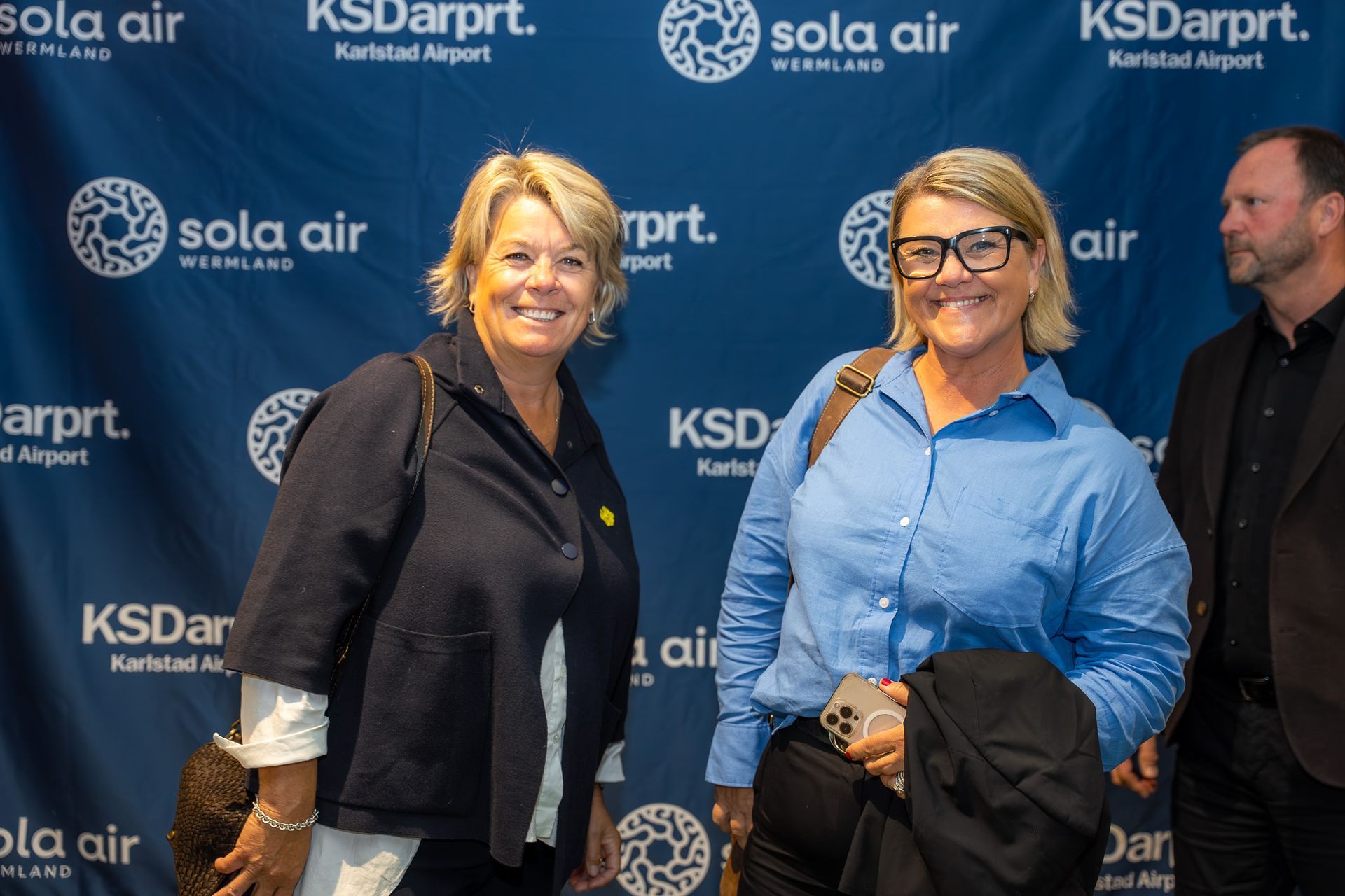 Två kvinnor poserar i bakgrunden av ett KSDartpt- och Sola Air-evenemang