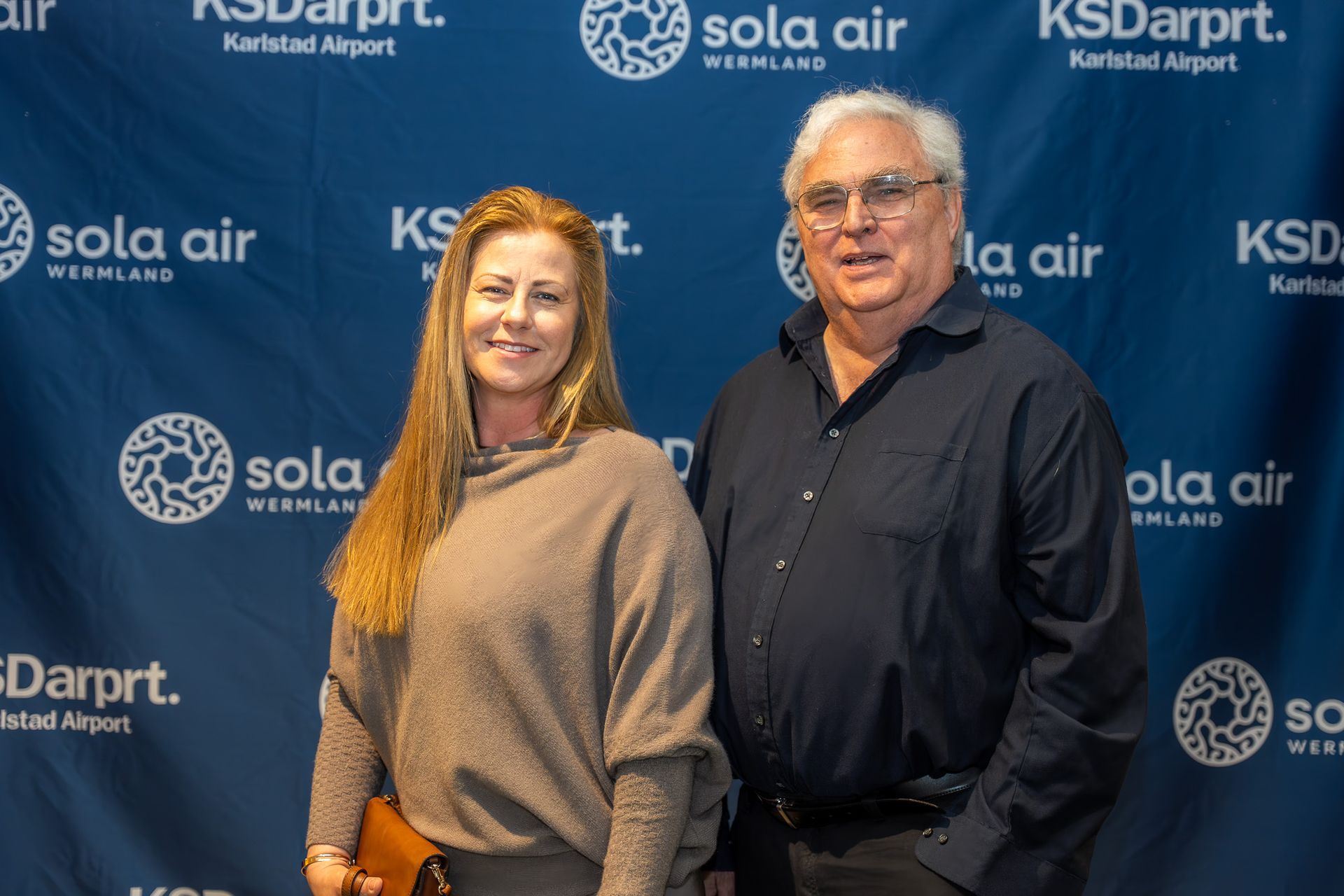 Två personer poserar framför en blå KSD-flygplats och Sola Air som bakgrund