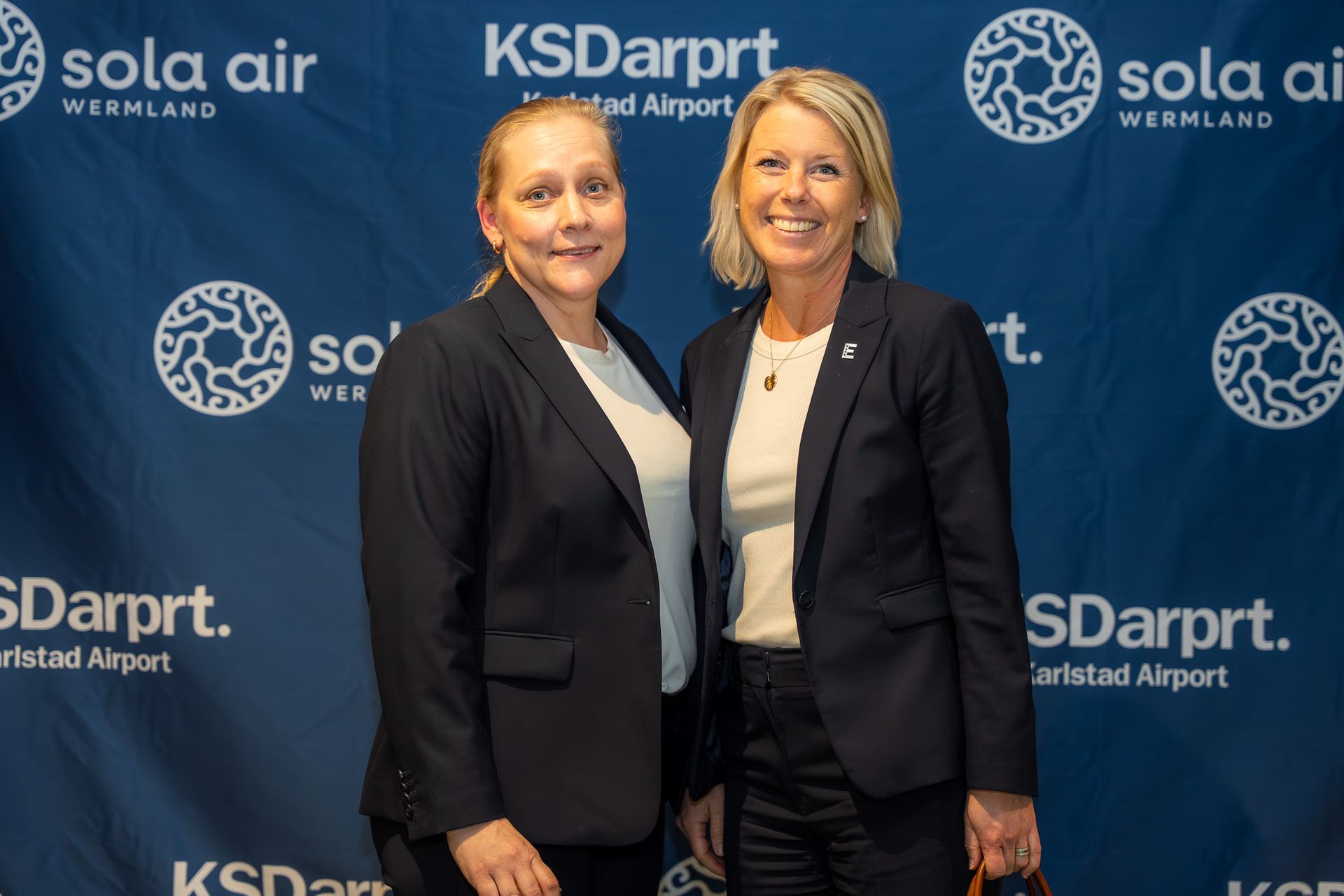 Två kvinnor i mörka kavajer poserar inför en KS Darpt- och Sola Air-konferens.