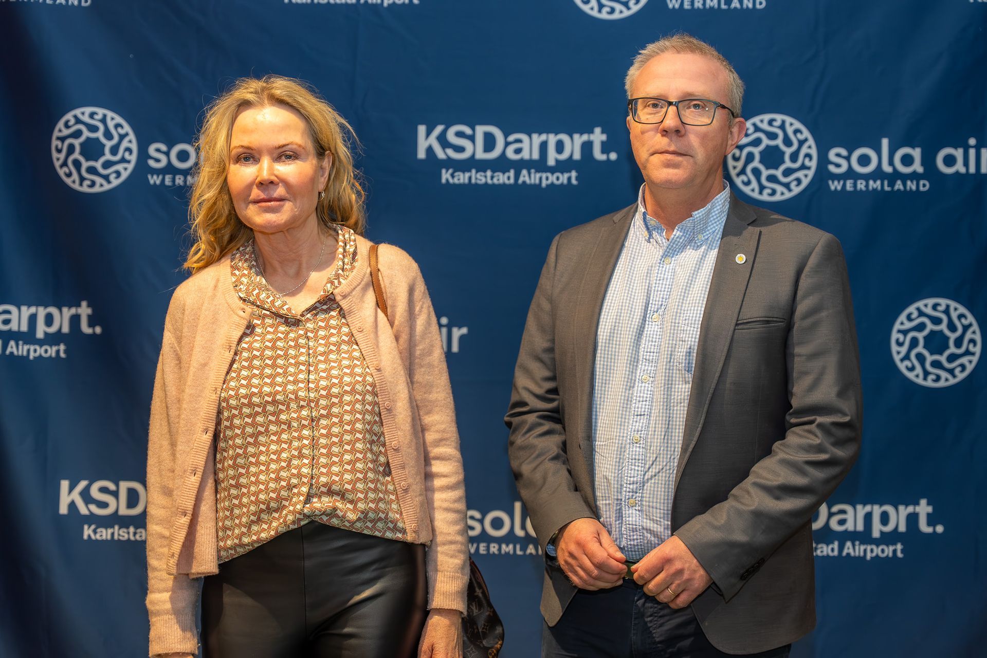 Två personer står framför en KSD Airport och Sola-logotypen i bakgrunden vid ett medieevenemang
