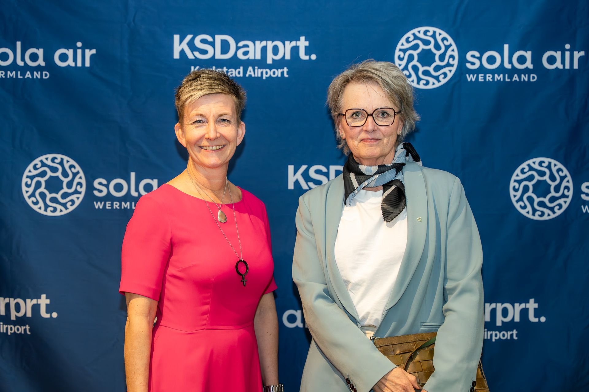 Två kvinnor poserar framför en blå KSD Airport och Sola Air-bakgrund