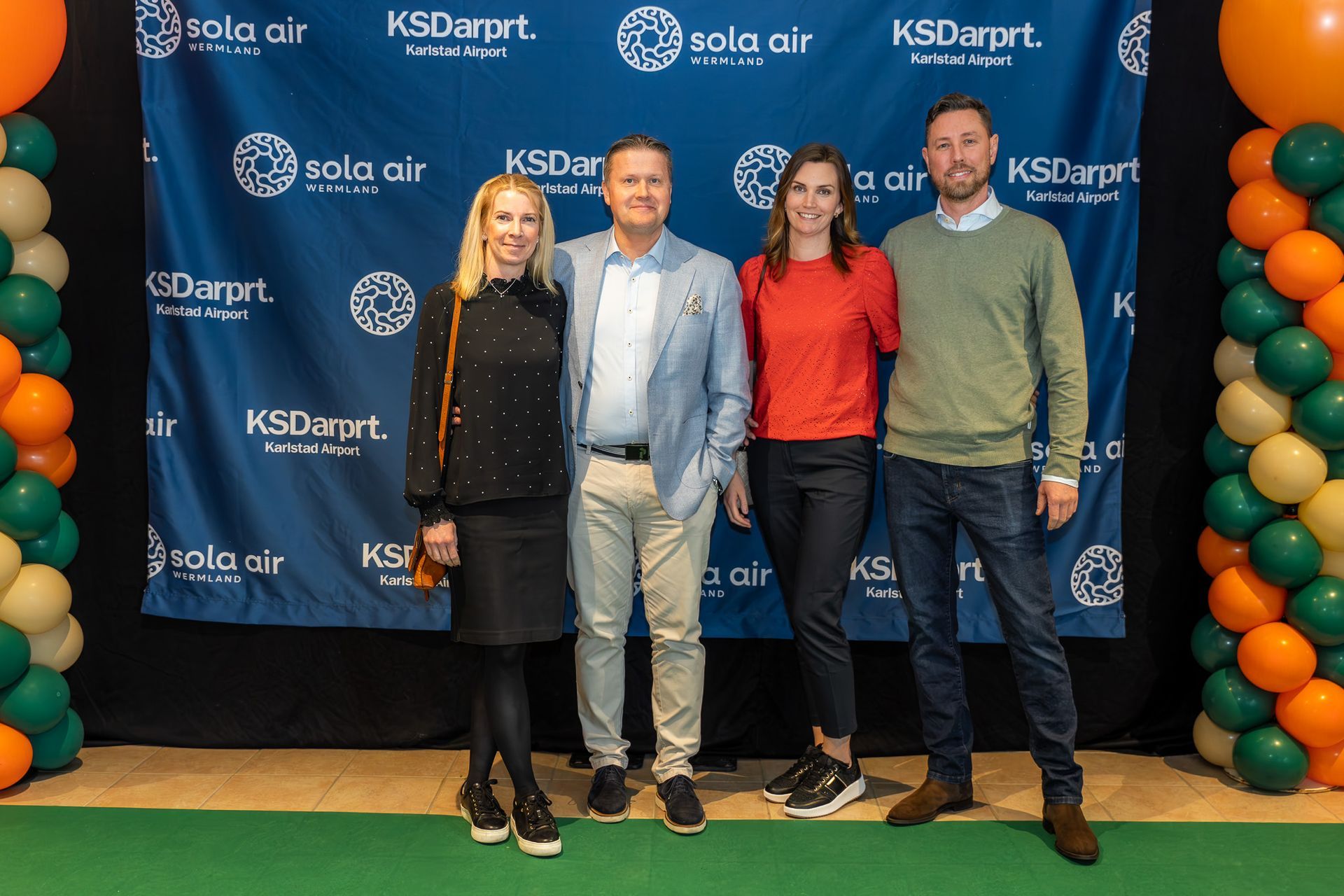 Fyra personer poserar framför en KSDartp/Sola air-bakgrund vid ett evenemang med grönt golv.