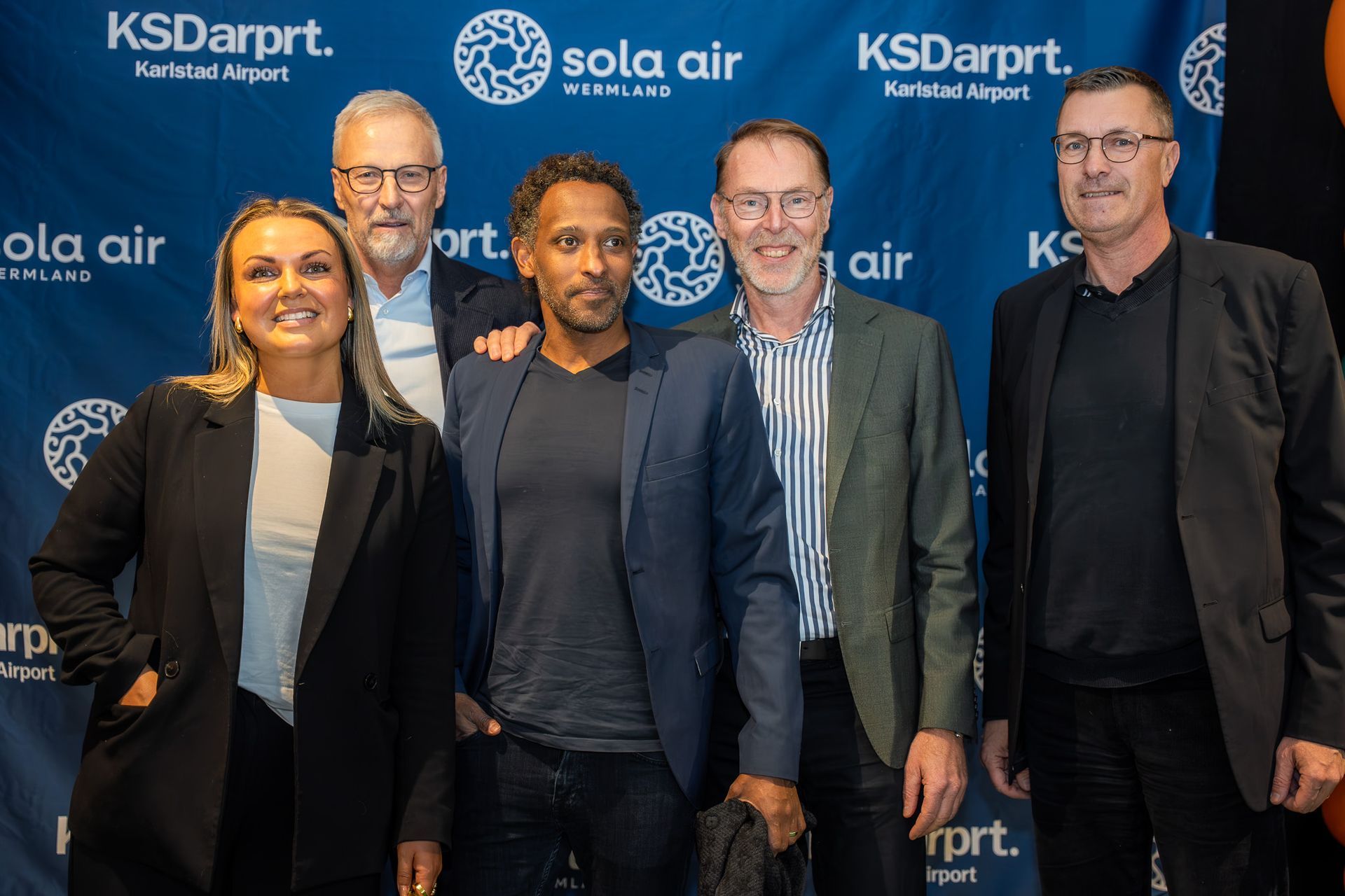 Fem personer poserar i affärskläder vid en evenemangsmiljö för KS Darpt och Sola Air.