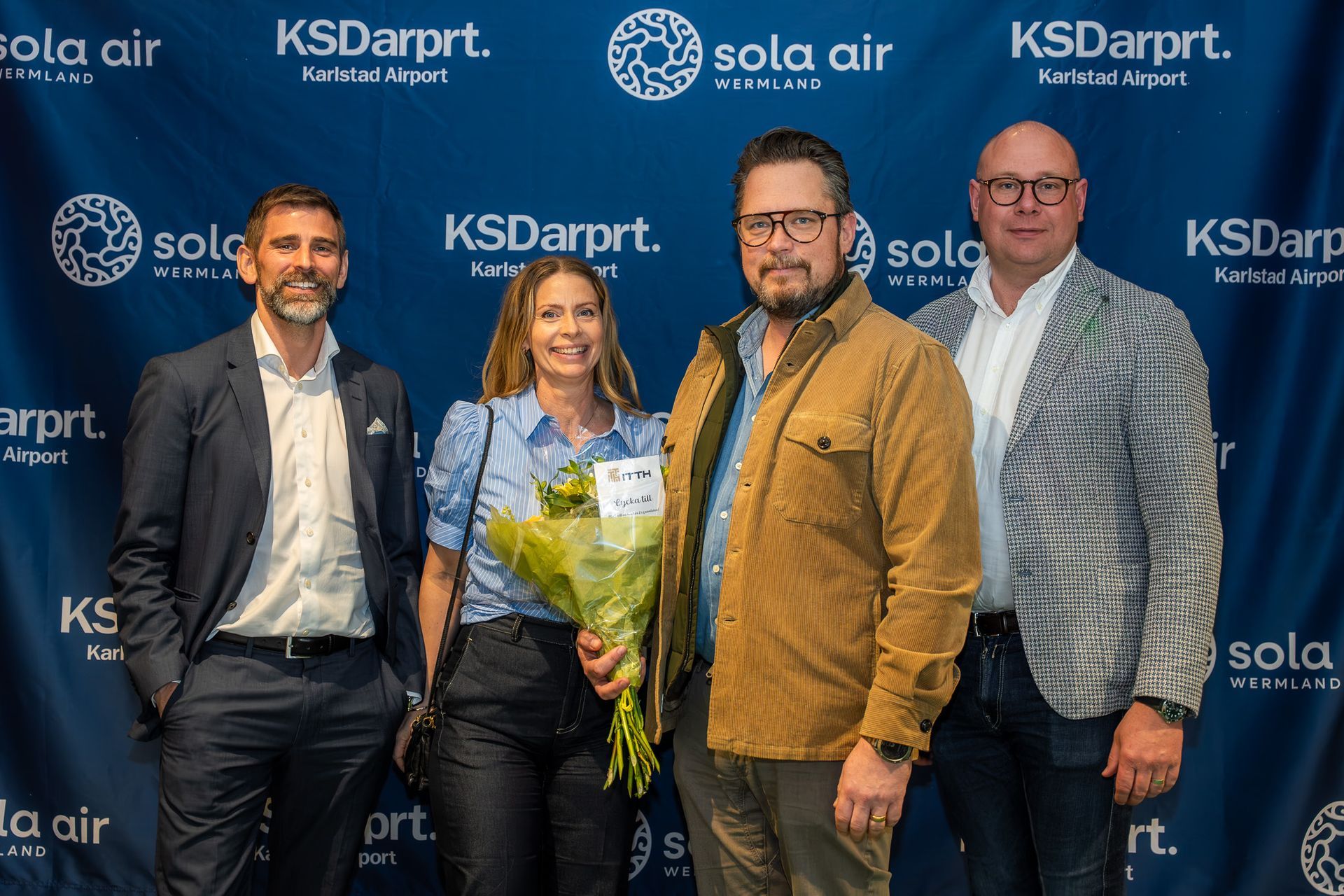 Fyra personer poserar på en blå steg-och-repeat-bakgrund med KSDarprt.- och Sola Air-logotyperna