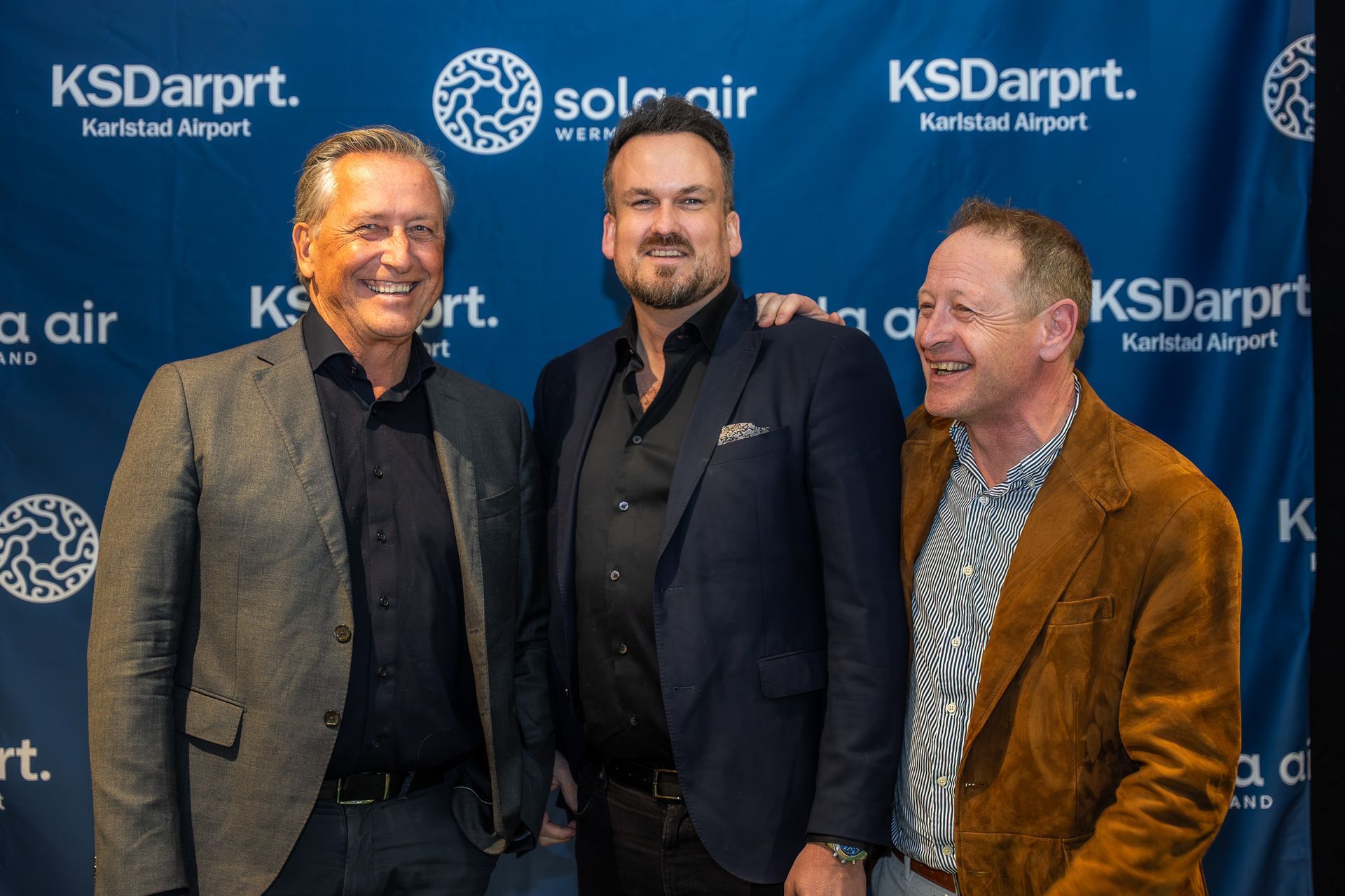 Tre leende män poserar framför en bakgrund med KSDarprt- och Solar Air-logotyp på ett evenemang