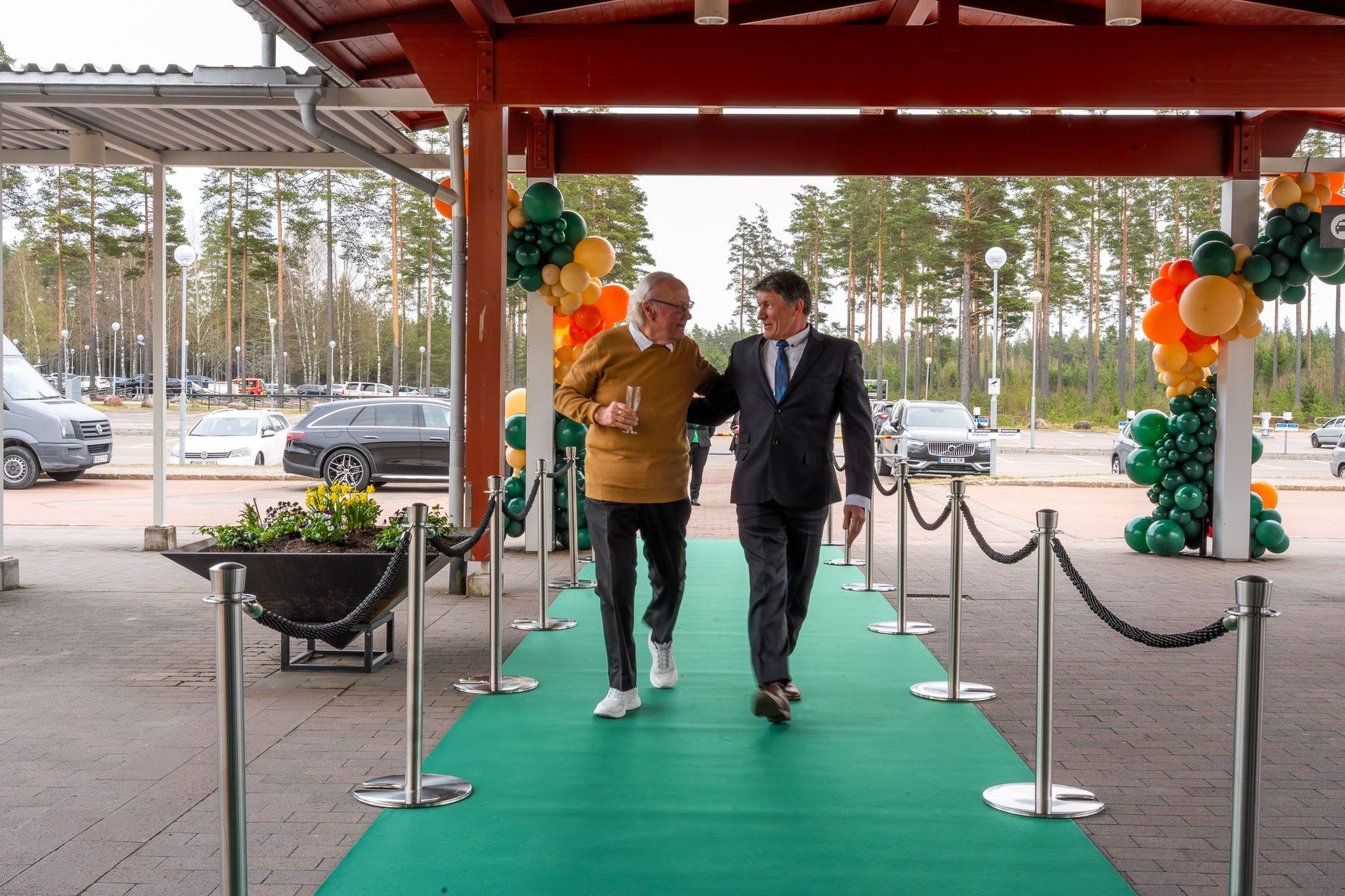 Två personer som går under en dekorerad entrébaldakin med grön matta och ballongbågar