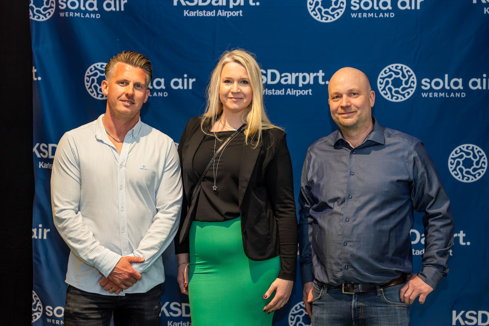 Tre personer poserar framför en blå Sola Air- och KSDarpit-bakgrund