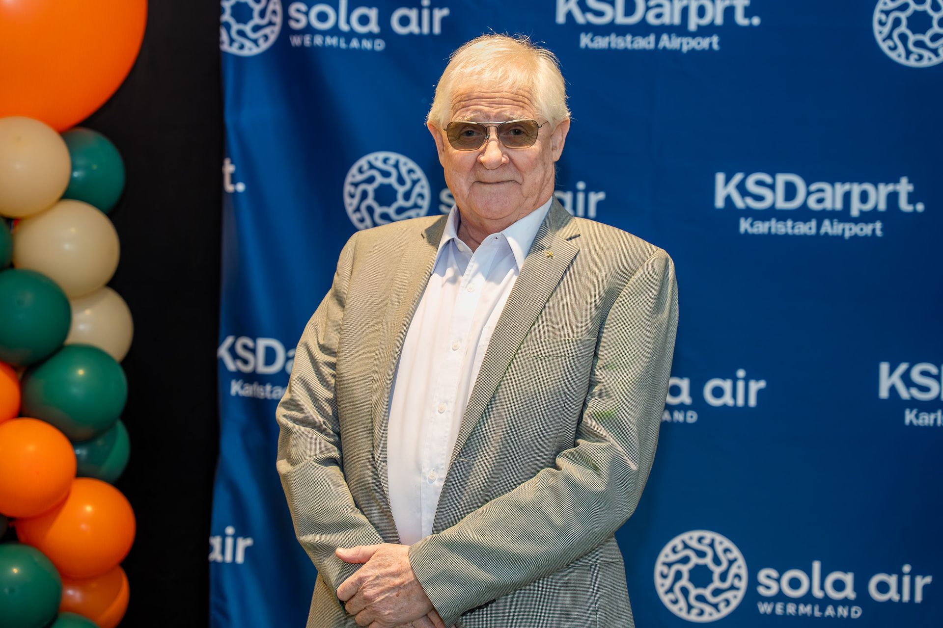 Man står i en ljus kavaj framför en KSDarpt. och Sola Air-bakgrund vid en ceremoni