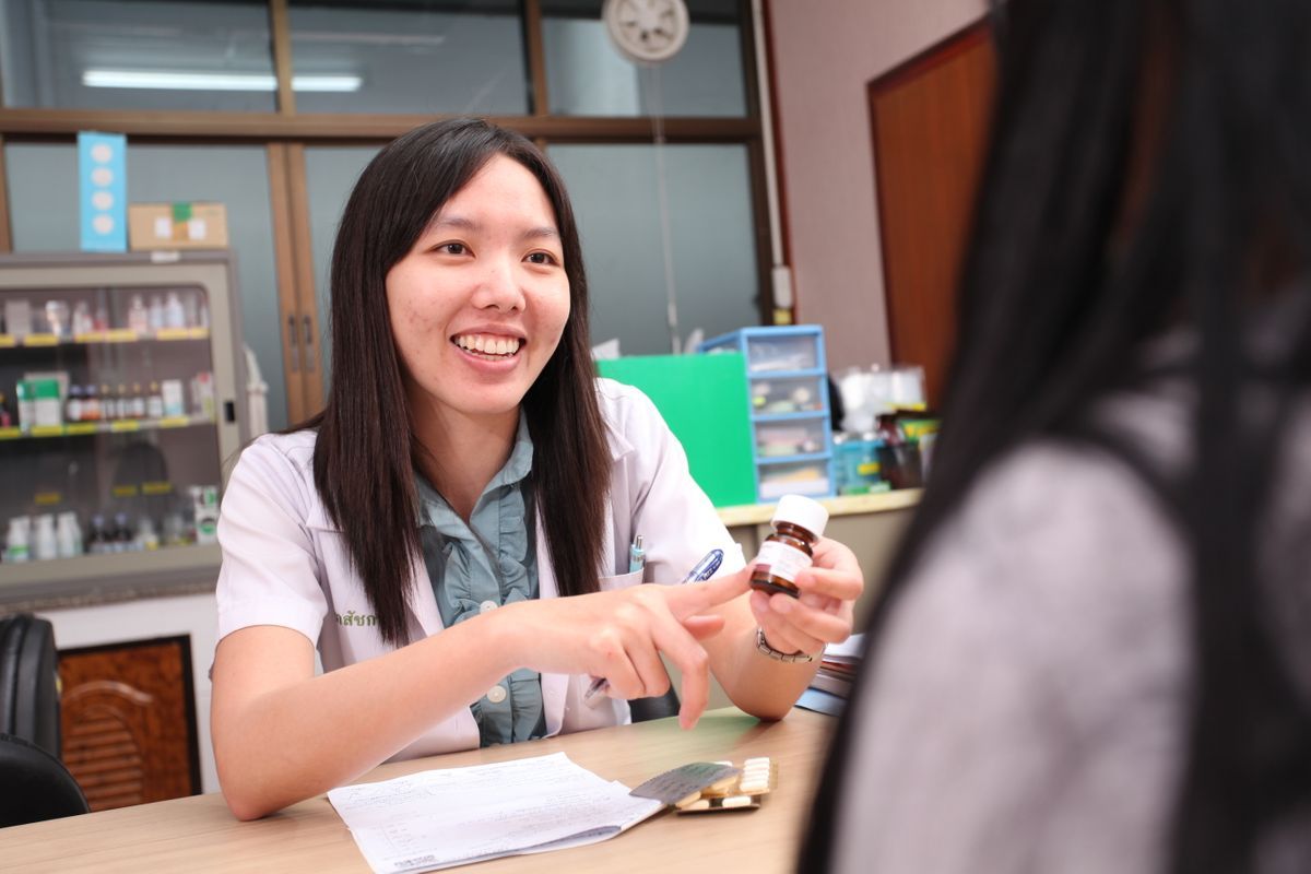 Pharmacist smiling, explaining medication to a customer at a pharmacy counter.